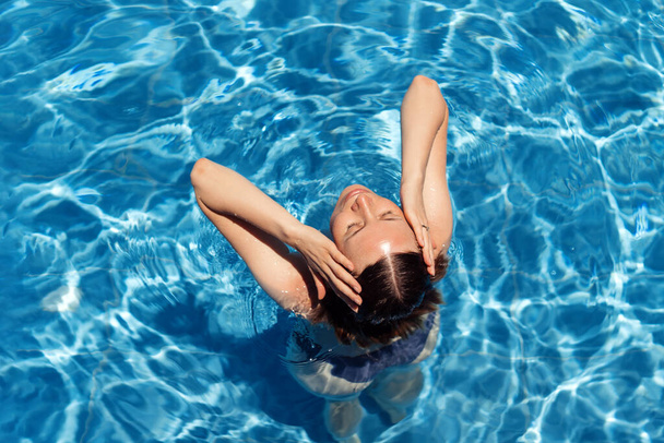 Γυναίκα βγαίνει από το νερό της μπλε πισίνας σε εξωτερικούς χώρους - Φωτογραφία, εικόνα