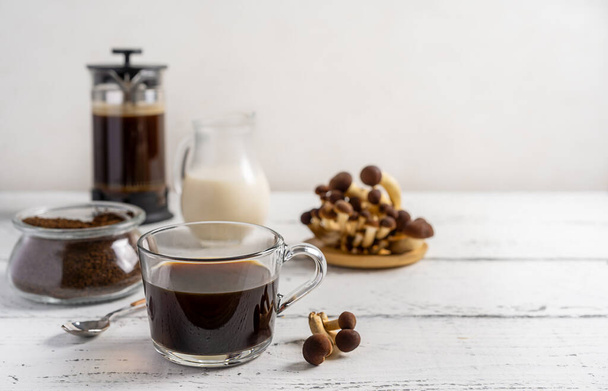 Healthy trendy coffee with mushrooms in cup, coffee pot, milk on white wooden background - Foto, afbeelding