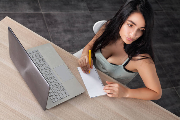 Brunetka dívka sedne na stůl a pracovat s notebookem  - Fotografie, Obrázek