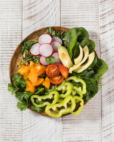 Vegetable summer salad with avocado, seasonal vegetables, spinach and micro-greens on a wooden white background.  - Photo, Image