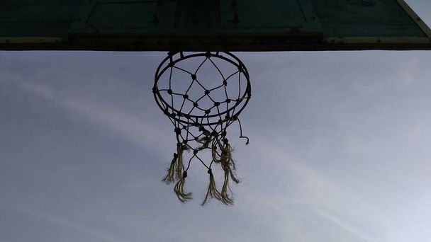 Első-hátsó szög kilátás homályos zöld régi kosárlabda karika és törött háló kék hátterű reggeli ég a nyilvános sportpályán. - Fotó, kép