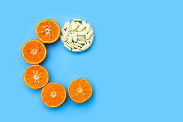 Pastillas de vitamina C con cítricos naranjas frescas aisladas sobre fondo azul. - Foto, imagen