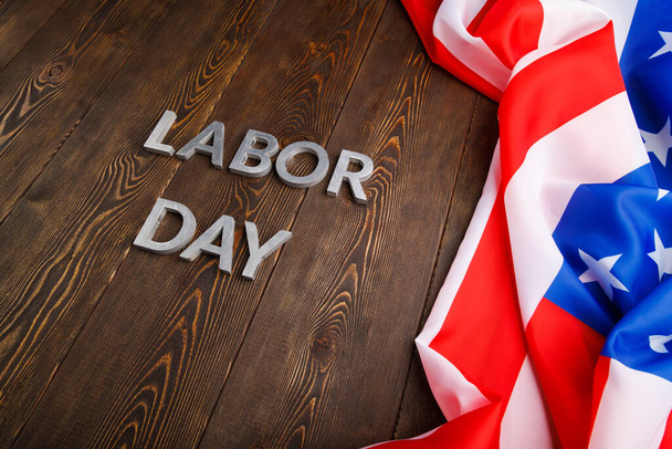 words labor day laid with silver metal letters on wooden surface with crumpled USA flag on left side - Fotó, kép