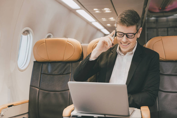 Uomo d'affari che utilizza Internet via satellite su laptop e telefono che chiama il contatto aziendale durante il volo aereo sorridere felice. - Foto, immagini