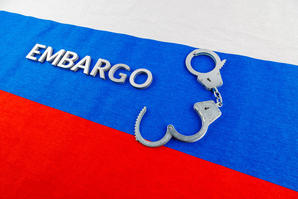 the word embargo laid with silver metal letters on russian tricolor flag with silver handcuffs - Zdjęcie, obraz