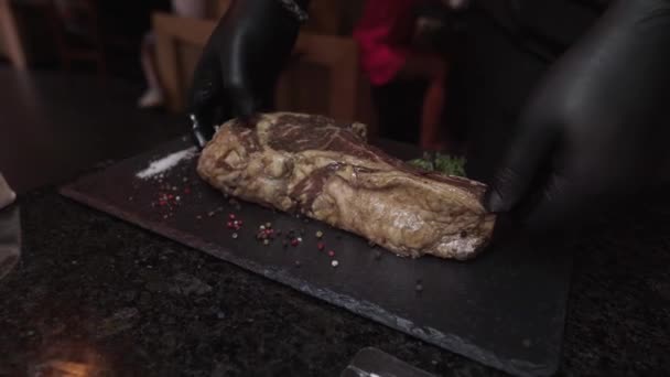 Šéfkuchař umístí velký syrový tomahawk steak na stojan na gril zabudovaný do stolu v restauraci. Vynikající kus starého masa. Grilování hovězího. - Záběry, video