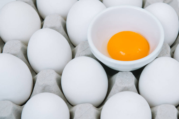 Białe surowe jaja kurze i samotnie rozbite brązowe jajko na tacy widok z góry - Zdjęcie, obraz