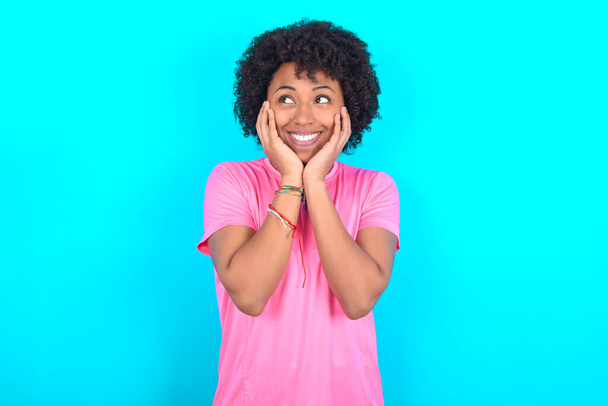 Inspired Young African American woman wearing pink T-shirt over blue background looking at copyspace having thoughts about future events - Photo, image