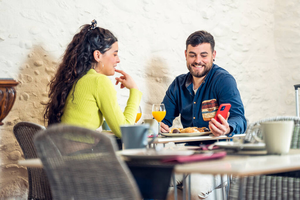 Τουριστικό ζευγάρι κοιτάζοντας το τηλέφωνο και το πρωινό σε ένα εστιατόριο του ξενοδοχείου - Φωτογραφία, εικόνα