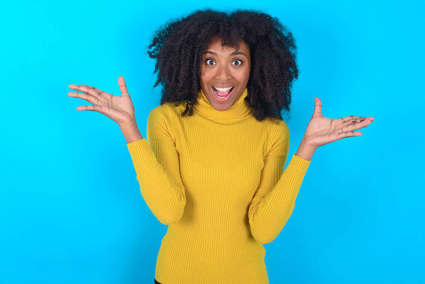 Afroameričanka v žlutém roláku na modrém pozadí slaví šílené a ohromený úspěch s rukama zvednutýma a otevřené oči křičí vzrušeně. Koncept vítěze - Fotografie, Obrázek