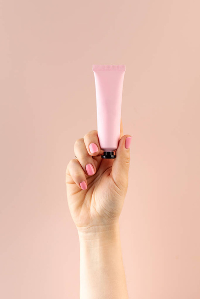 Mockup of a pink tube with a cosmetic product in a female hand on a light pink background. Beauty product concept. - Foto, Bild