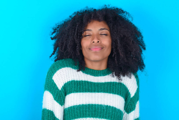 African American woman wearing striped sweater over blue background nice-looking sweet charming cute attractive lovely winsome sweet peaceful closed eyes - Фото, зображення