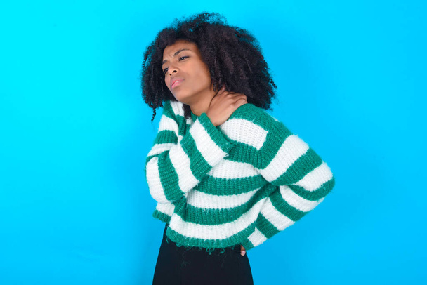 African American woman wearing striped sweater over blue background got back pain - Foto, Bild