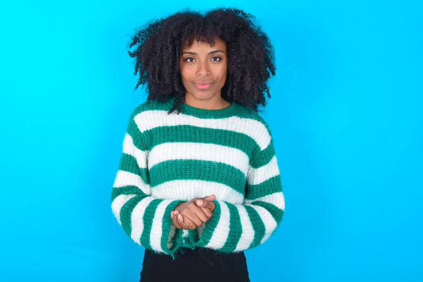 Foto di allegra donna afroamericana sicura di sé che indossa maglione a righe su braccia sfondo blu insieme - Foto, immagini