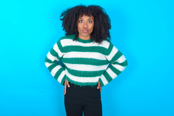 Portrait of lovely funny African american woman wearing striped sweater over blue background sending air kiss - Photo, Image