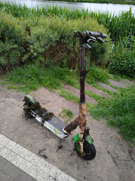 Scatto verticale di uno sporco scooter elettrico fangoso tirato fuori dal lago. Concetto di pericolo ecologico. - Foto, immagini