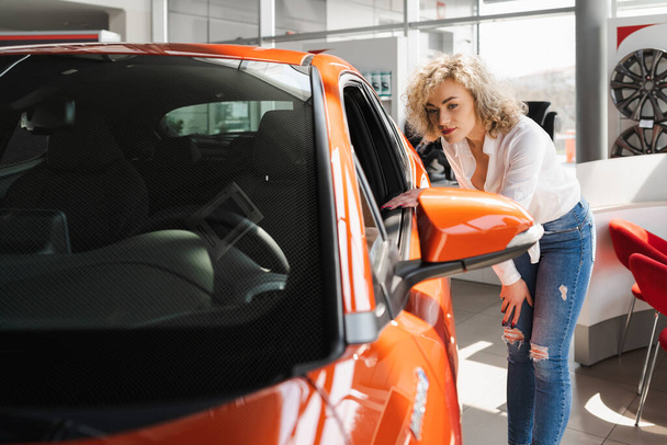 Curly blonde in a car dealership. Woman chooses a new car - Фото, изображение