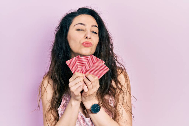 Giovane donna ispanica che copre la bocca con le carte guardando la fotocamera che soffia un bacio di essere bella e sexy. espressione d'amore.  - Foto, immagini