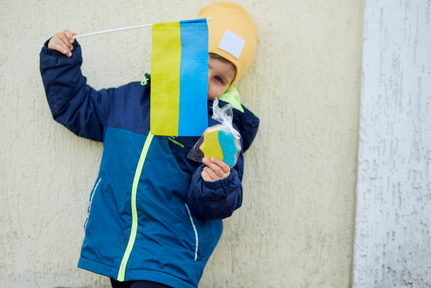 Patriotischer kleiner Junge hält ukrainische Flagge und symbolische Kekse in der Hand. Steht zur Ukraine. Unterstützt die Ukraine. Stoppt das russische Aggressionskonzept. Stoppt den Krieg in der Ukraine. Betet für die Ukraine - Foto, Bild