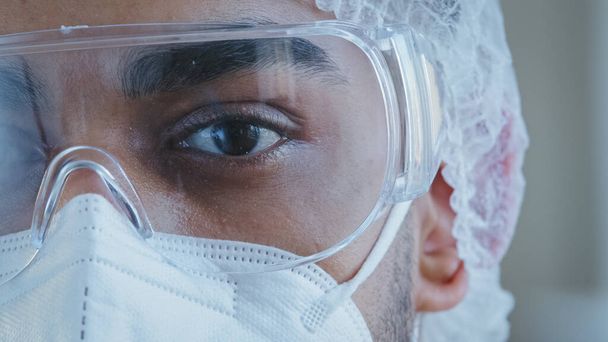 Close up male black tired and sleepy eye half face man doctor wearing personal protective glasses medical special clothing uniform working in hospital looking at camera coronavirus covid-19 epidemic - Fotoğraf, Görsel