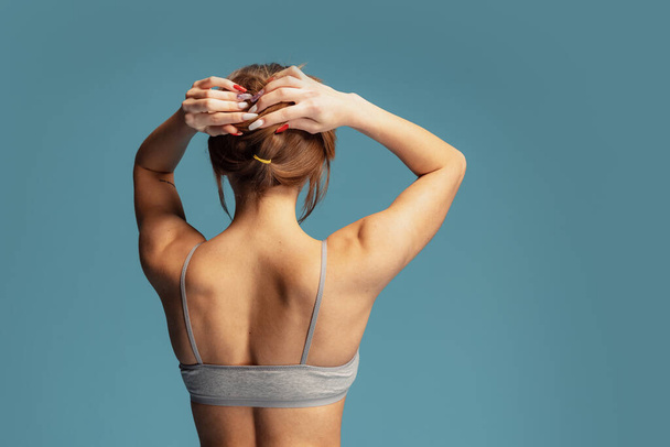 Strong back. Half-length image of beautiful sportive female back, shoulders isolated over blue background - Fotografie, Obrázek