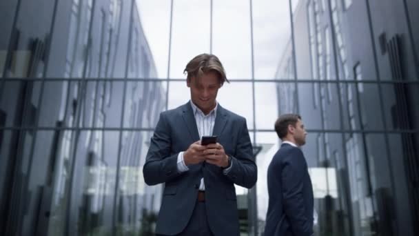 Hombre de negocios sonriente sosteniendo teléfono inteligente en el moderno edificio de oficinas. Zona centro - Metraje, vídeo
