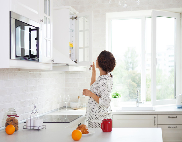 Femme préparant une tasse de café dans sa cuisine portant un pyjama
 - Photo, image