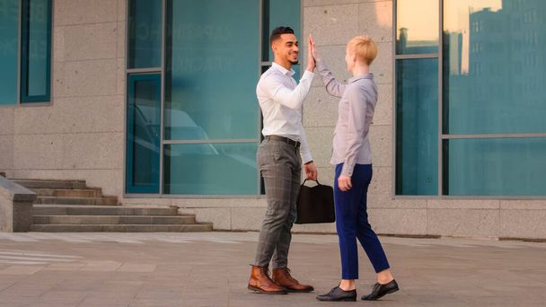 Dva přátelští multiraciální kolegové obchod co-workers arabský hispánec muž a běloška žena setkat venku na ulici dělat high five hands gesto neformální pozdrav jít pryč v různých přímých - Fotografie, Obrázek