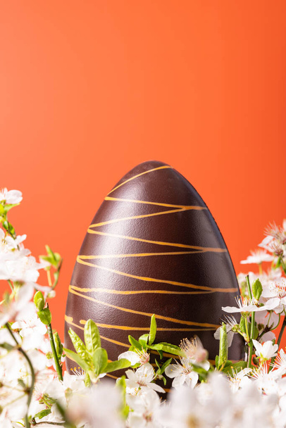 鮮やかなオレンジ色の背景に春の花とイースターチョコレートの卵 - 写真・画像