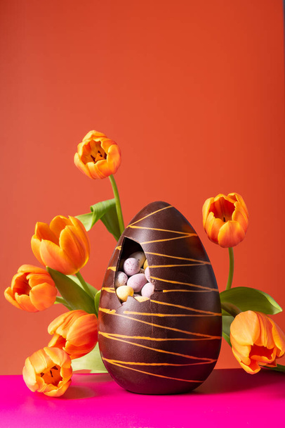 Huevo de chocolate de Pascua con tulipanes de primavera sobre fondo naranja vibrante - Foto, imagen