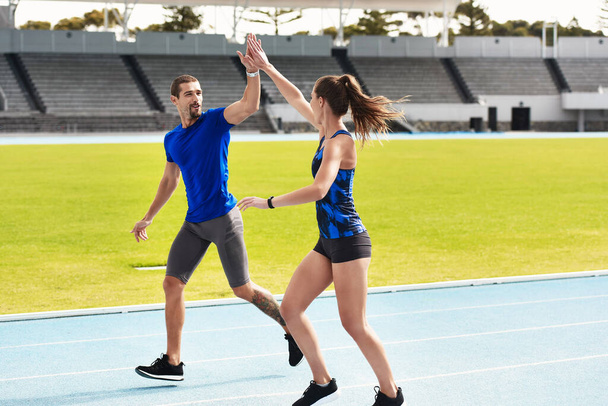 Good job. Full length shot of two young athletes high fiving while running along the track. - 写真・画像