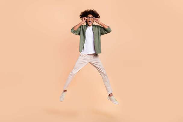 Full length body size view of attractive cheerful guy jumping touching specs isolated over beige pastel color background - Foto, Bild