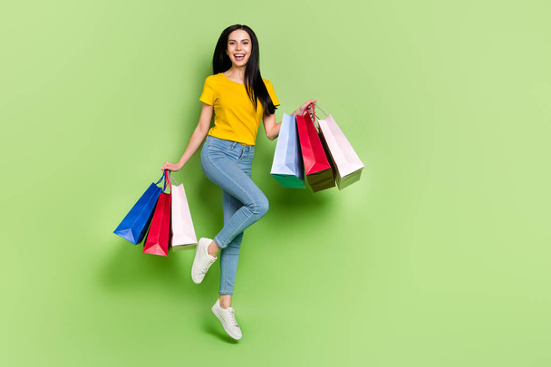 Full length photo of cheerful crazy girl hold packages energetic jumping isolated on green color background - Foto, Imagen