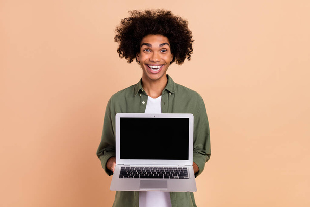 Portrait of attractive cheerful amazed trendy wavy-haired guy holding laptop copy space isolated over beige pastel color background - Φωτογραφία, εικόνα