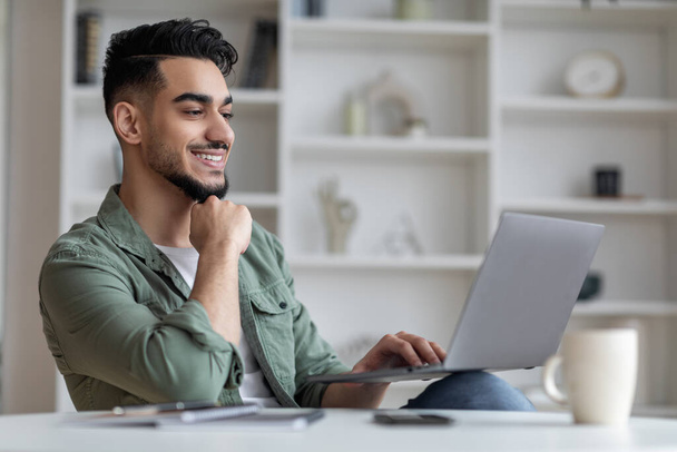 Ritratto di bello sorridente giovane arabo sul computer portatile a casa ufficio - Foto, immagini