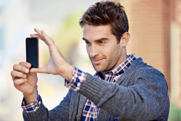 Phone photography. Shot of a handsome young man taking a photograph with his mobile phone phone outdoors. - Photo, image