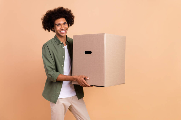 Portrait of attractive cheerful wavy-haired guy carrying paper box new life isolated over beige pastel color background - Foto, Imagen