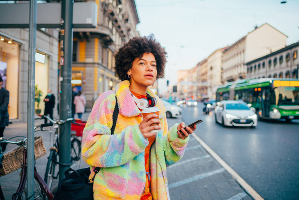 Jeune femme bouclée noire en plein air tenant tasse réutilisable takeway café pour aller à l'aide d'un smartphone - Photo, image