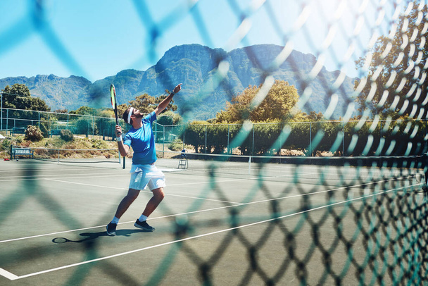 Getting the perfect serve. Full length shot of a handsome young sportsman playing tennis alone on a court during the day. - 写真・画像