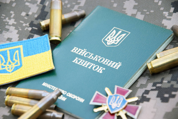 Ukrainischer Militärausweis auf dem Hintergrund militärischer Tarnung, umgeben von Granaten und nationalen Symbolen. Krieg in der Ukraine. Krieg beenden. - Foto, Bild