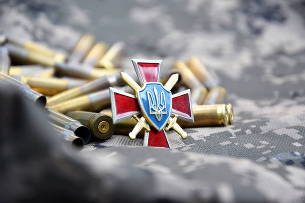 Ukrayna 'nın kara kuvvetlerinin rozeti askeri kamuflajın arka planına karşı bombardımanla çevrili. Ukrayna 'da savaş. Savaşı durdurun.. - Fotoğraf, Görsel