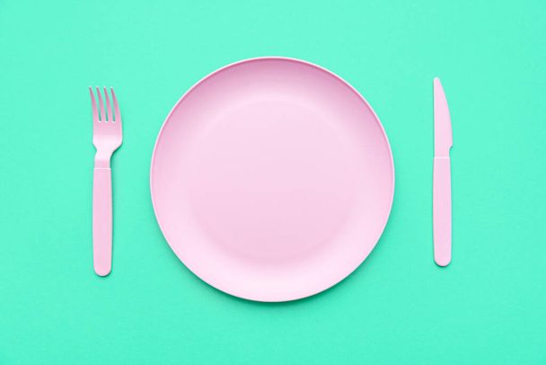 Prázdný talíř izolovaný na zeleném pozadí. Růžové příbory na zeleném stole, pohled shora. - Fotografie, Obrázek