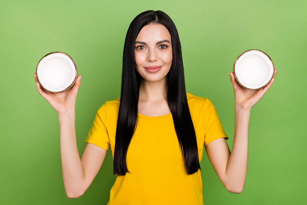 Portrait of gorgeous satisfied person hold two half coconut isolated on green color background - Foto, Bild