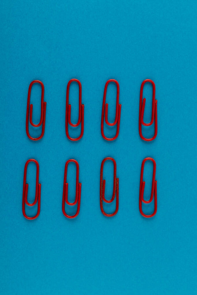 Colored paper clips. Red paper clips macro close up isolated on a blue background with copy space. - Фото, изображение