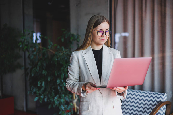 Női adminisztratív menedzser szemüvegben és formális öltöny séta az irodába digitális laptop, hogy ellenőrizze az irodai munkafolyamat, magabiztos női üzleti tulajdonos - Fotó, kép