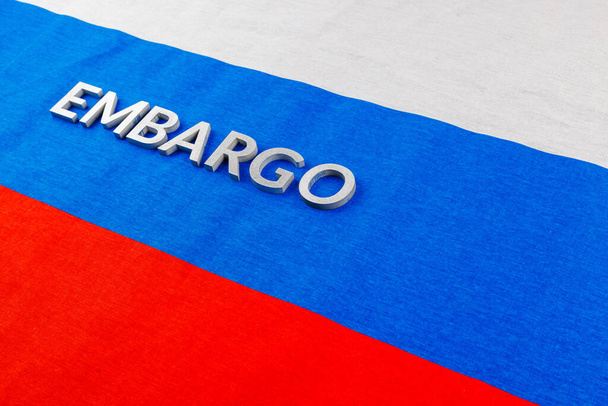 the word embargo laid with silver metal letters on russian tricolor flag in diagonal view - Photo, Image