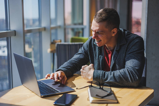 Portrait of a man, IT professional, working remotely with a modern laptop, sitting at a table and smiling at the camera during a break, a happy human programmer in vision correction glasses - Photo, Image