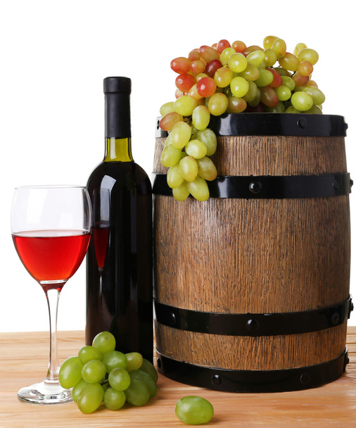 Wine in goblet and in bottle, grapes and barrel on wooden table on white background - Фото, зображення