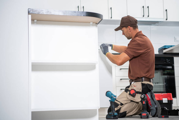 Caucasian Cabinetmaker Contractor Worker in His 40s Finishing Installation of a New Kitchen Cabinets Inside an Apartment. - Photo, image