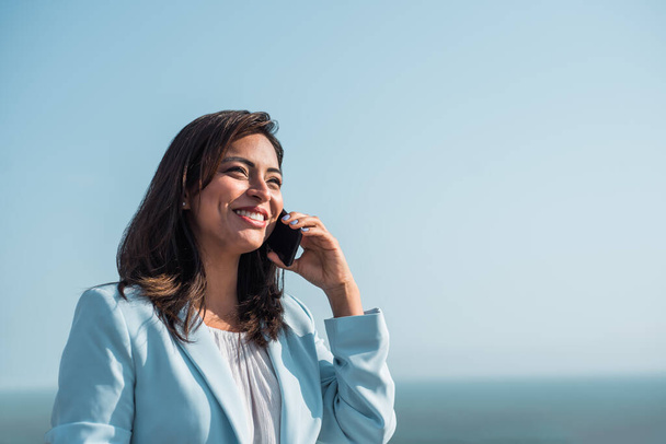 Glückliche Geschäftsfrau telefoniert im Freien mit Küstenhintergrund, himmlischem Himmel. Kopierraum - Foto, Bild